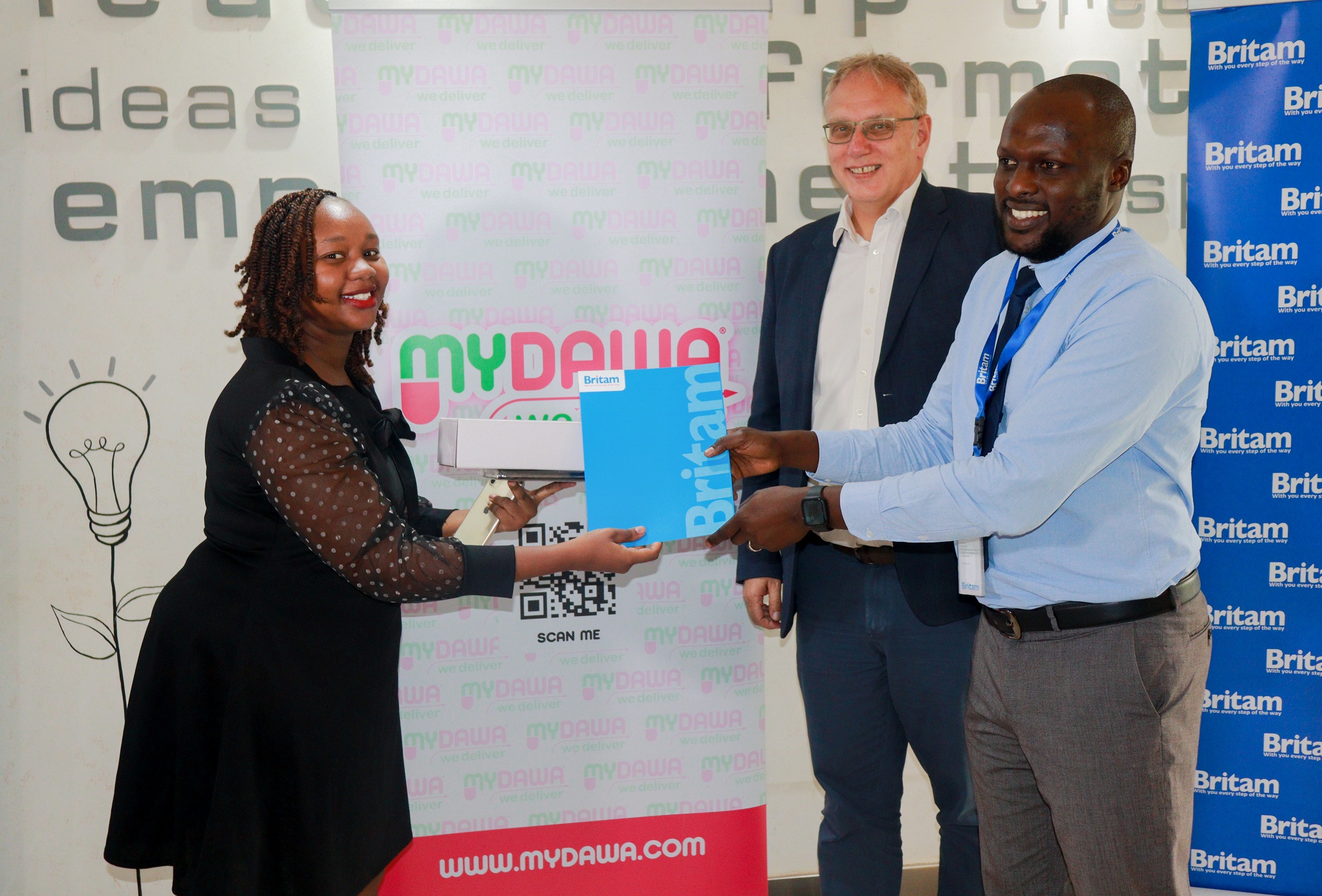 Britam GM in Charge of Health David Obonyo presenting the Ksh 1 million Milele Health Plan policy Cover to the Pink Friday Campaign winner Martha Murugi. Looking on is MYDAWA MD Tony Wood